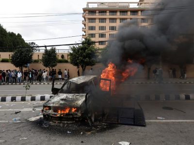 Orang-orang berdiri di dekat sebuah kendaraan yang dibakar oleh para demonstran saat aksi protes menentang korupsi dan keputusan pemerintah memblokir sejumlah platform media sosial, di Kathmandu, Nepal, 8 September. Sumber foto : REUTERS